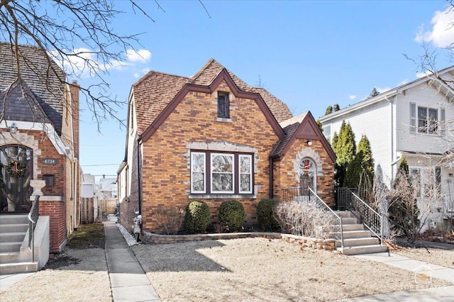 tudor house featuring fence, brick siding, and a shingled roof