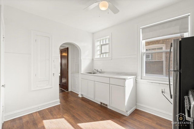 kitchen with light countertops, dark wood-style flooring, freestanding refrigerator, arched walkways, and a sink