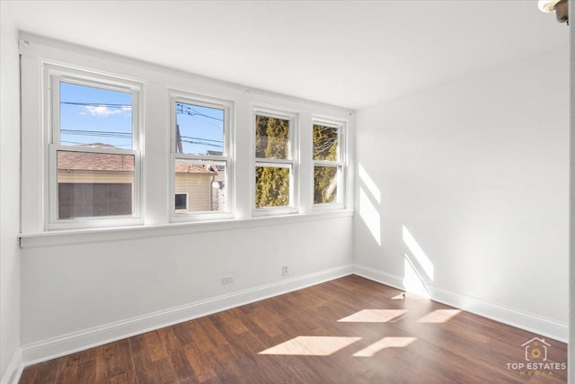 spare room featuring baseboards, a healthy amount of sunlight, and dark wood-style flooring
