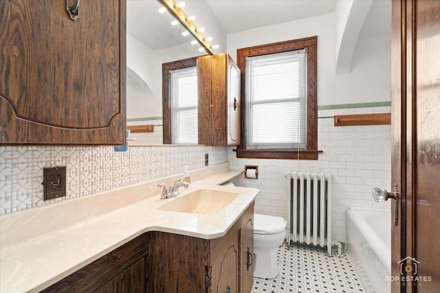 bathroom featuring vanity, a tub to relax in, radiator heating unit, tile walls, and toilet