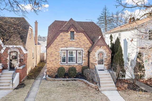 tudor home featuring brick siding and a shingled roof