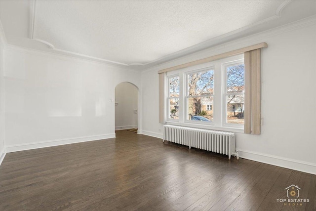 spare room with wood finished floors, arched walkways, radiator, crown molding, and baseboards