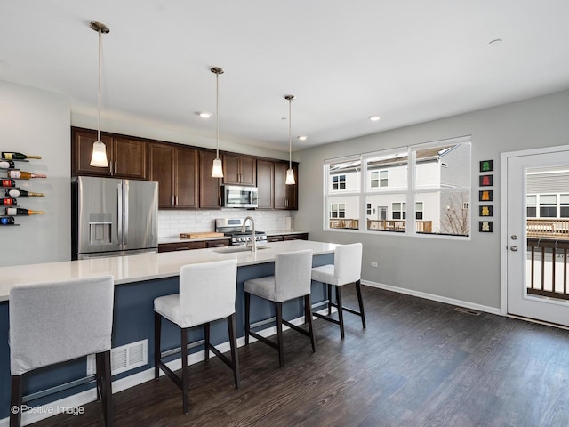 kitchen featuring dark wood-style floors, light countertops, dark brown cabinets, appliances with stainless steel finishes, and tasteful backsplash