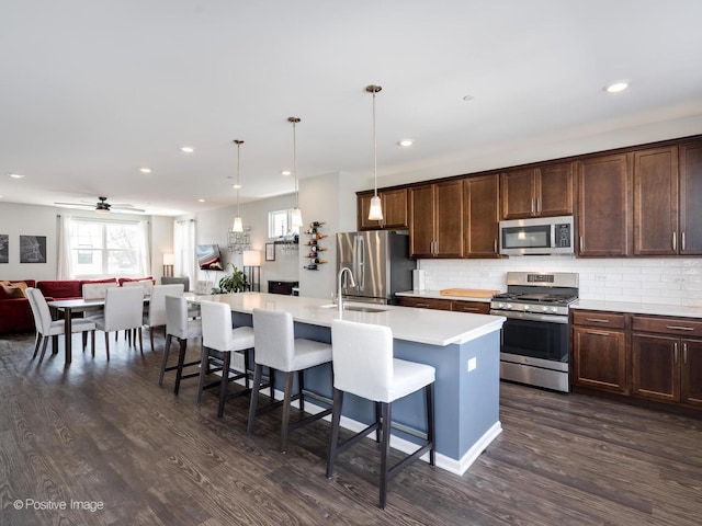 kitchen with tasteful backsplash, open floor plan, a breakfast bar, an island with sink, and appliances with stainless steel finishes