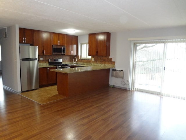 kitchen featuring stainless steel appliances, wood finished floors, a peninsula, and tasteful backsplash