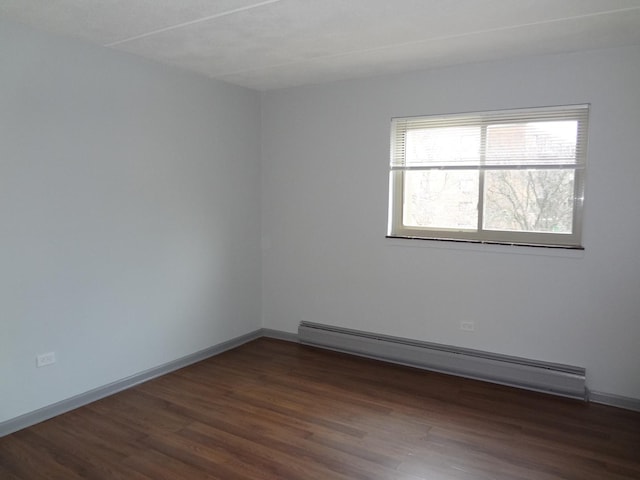 unfurnished room with a baseboard heating unit, dark wood finished floors, and baseboards