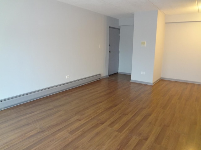 spare room with a baseboard heating unit, wood finished floors, and baseboards