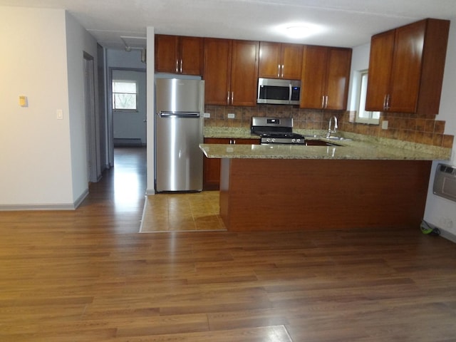 kitchen with stainless steel appliances, wood finished floors, backsplash, a sink, and light stone countertops