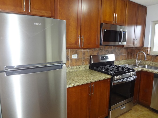 kitchen featuring appliances with stainless steel finishes, a sink, backsplash, and light stone countertops