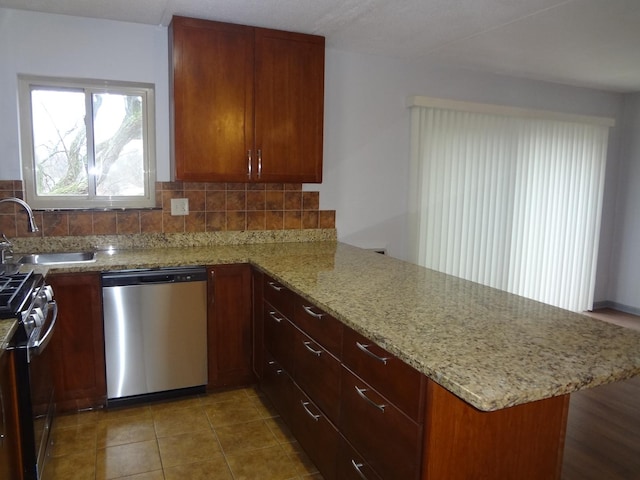 kitchen with light stone counters, stainless steel appliances, a peninsula, a sink, and decorative backsplash