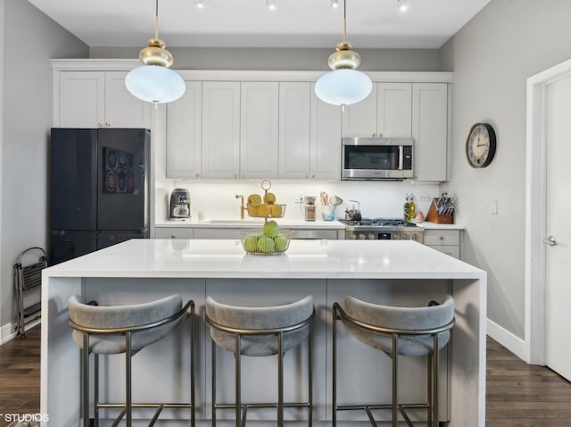 kitchen with range, stainless steel microwave, dark wood-type flooring, a center island, and freestanding refrigerator