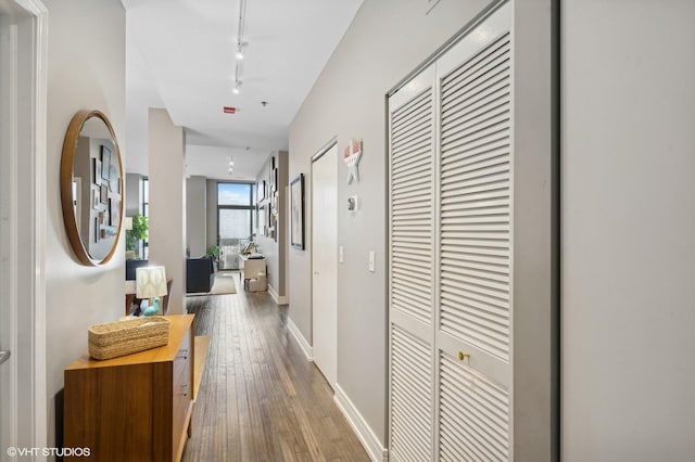 hallway featuring baseboards, track lighting, and hardwood / wood-style flooring