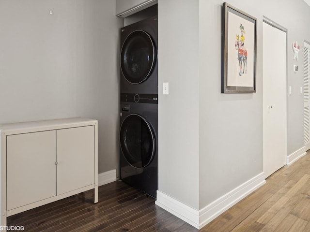 laundry area featuring laundry area, baseboards, stacked washer / drying machine, and wood finished floors