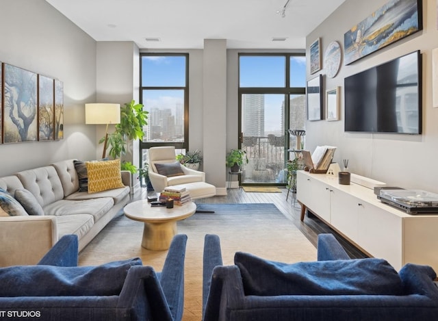 living area with a wall of windows, rail lighting, wood finished floors, and visible vents