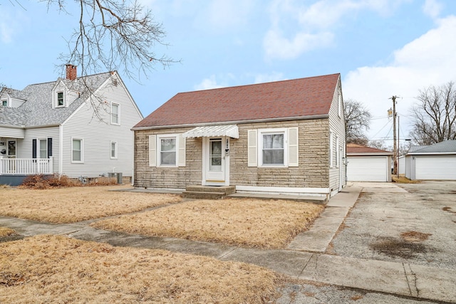 view of front of property featuring an outbuilding, stone siding, a shingled roof, and a detached garage