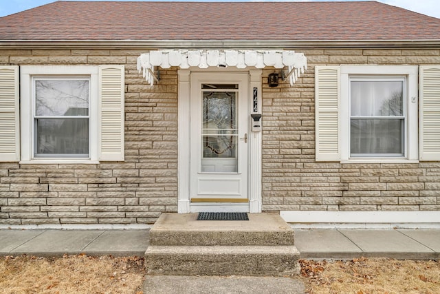 view of exterior entry featuring a shingled roof and brick siding