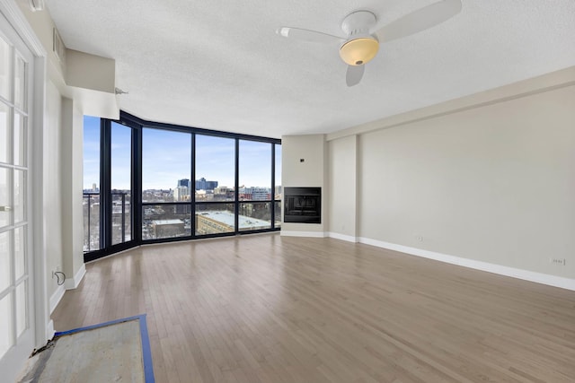 unfurnished living room with a view of city, light wood-style flooring, expansive windows, a fireplace, and baseboards