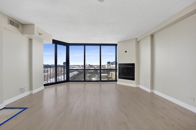 unfurnished living room with visible vents, wood finished floors, floor to ceiling windows, a fireplace, and baseboards