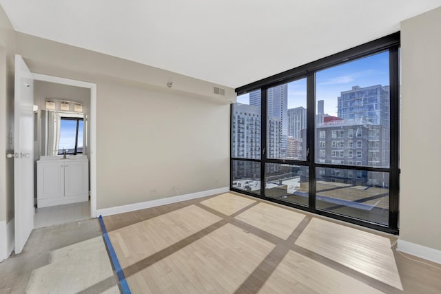 empty room featuring visible vents, a view of city, wood finished floors, floor to ceiling windows, and baseboards