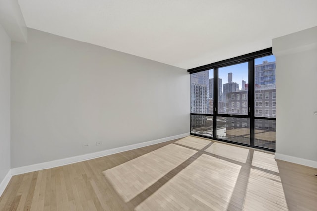 empty room featuring a city view, wood finished floors, baseboards, and expansive windows