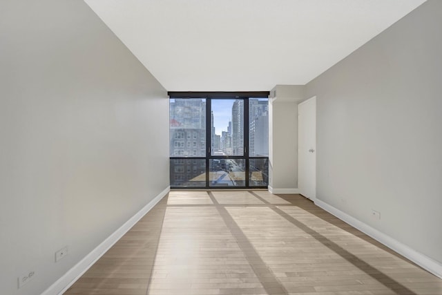 empty room featuring light wood-style flooring, a view of city, baseboards, and expansive windows