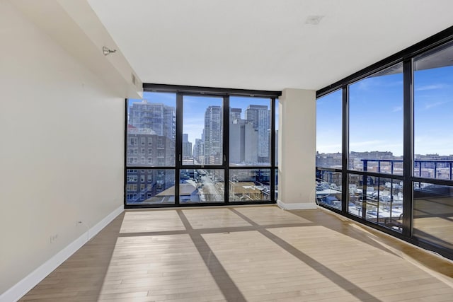 spare room with wood finished floors, baseboards, plenty of natural light, expansive windows, and a view of city