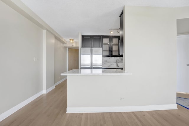 kitchen featuring glass insert cabinets, baseboards, light stone countertops, light wood-style flooring, and stainless steel refrigerator