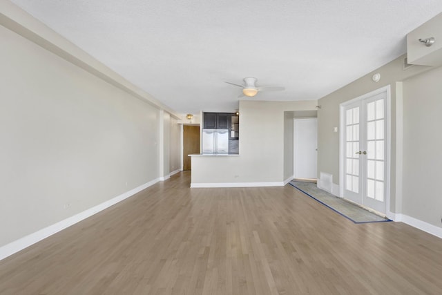 unfurnished living room with baseboards, ceiling fan, light wood-type flooring, french doors, and a textured ceiling