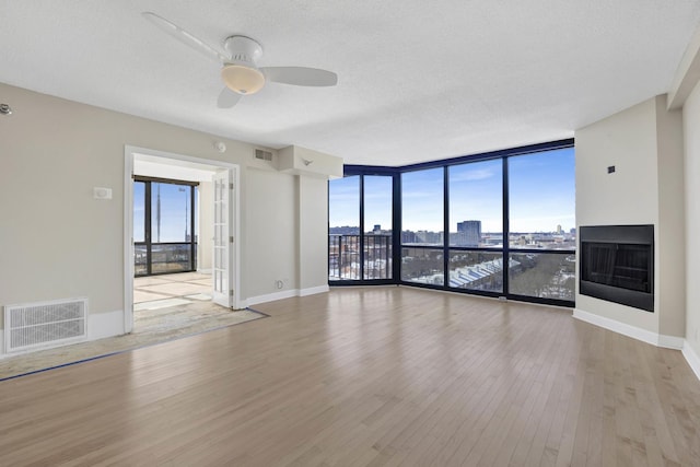 unfurnished room with visible vents, a city view, a wall of windows, and wood finished floors