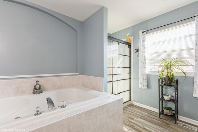 bathroom featuring a garden tub, wood finished floors, baseboards, and a shower stall