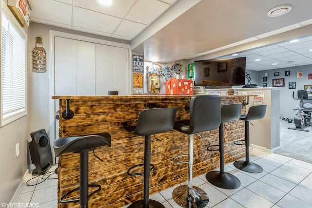 bar featuring a bar, light tile patterned floors, baseboards, and a drop ceiling