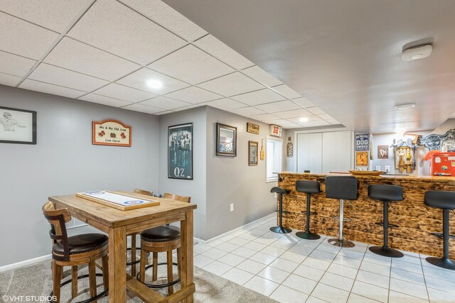 interior space featuring a bar, tile patterned floors, a paneled ceiling, and baseboards