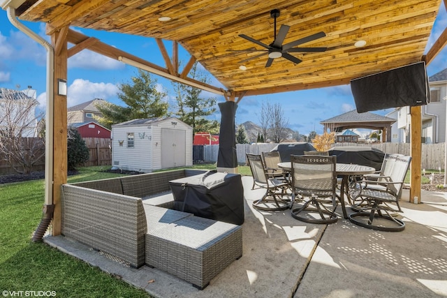 view of patio / terrace with a storage shed, a fenced backyard, outdoor dining area, an outbuilding, and a ceiling fan