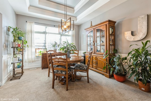 dining area with light carpet, wainscoting, a tray ceiling, and ornamental molding