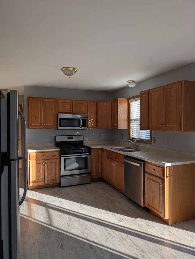 kitchen with brown cabinets, appliances with stainless steel finishes, light countertops, and a sink