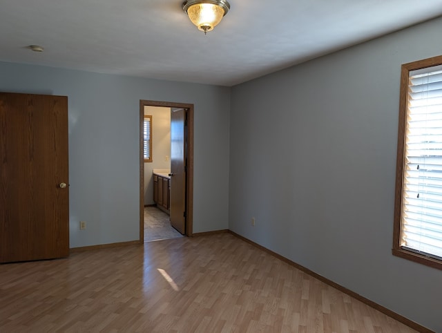 unfurnished bedroom featuring ensuite bathroom, light wood-style flooring, and baseboards