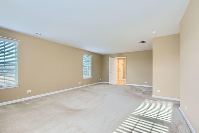 spare room with a healthy amount of sunlight, baseboards, visible vents, and light colored carpet