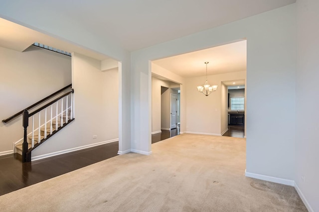 carpeted empty room featuring baseboards, an inviting chandelier, and stairs