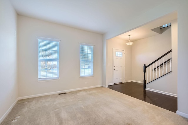 foyer featuring stairs, dark carpet, visible vents, and baseboards