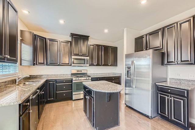 kitchen featuring appliances with stainless steel finishes, light wood-style floors, a sink, and light stone countertops