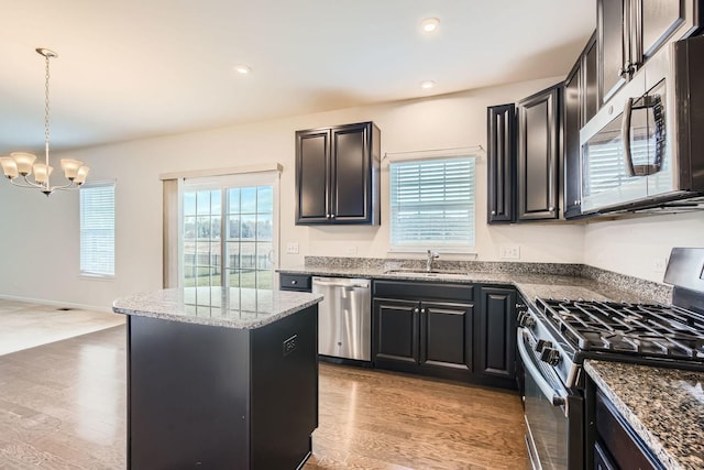 kitchen with light wood-style flooring, stainless steel appliances, a kitchen island, a sink, and dark cabinetry