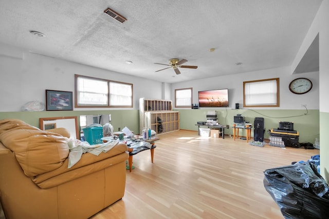 living area with a textured ceiling, light wood-style flooring, visible vents, and a ceiling fan