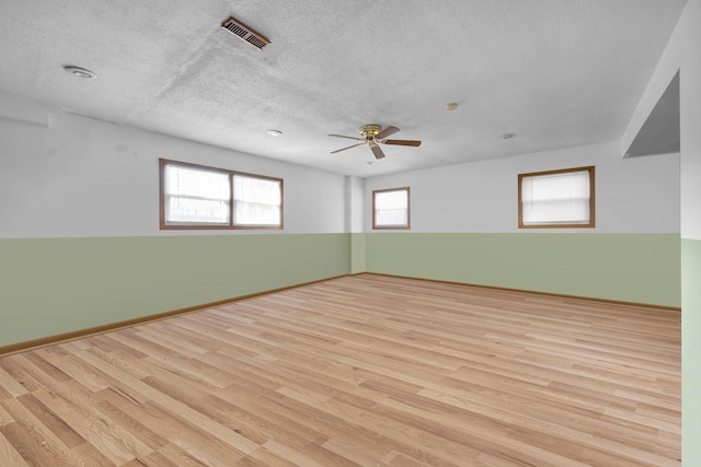 empty room with baseboards, visible vents, ceiling fan, wood finished floors, and a textured ceiling