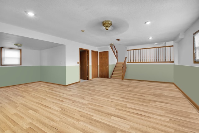 empty room with a textured ceiling, stairway, wood finished floors, and baseboards