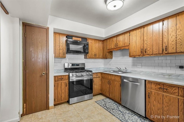 kitchen with brown cabinetry, stainless steel appliances, a sink, and light countertops