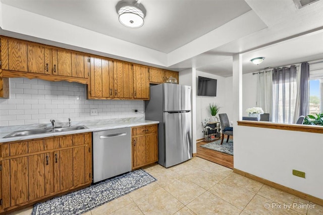 kitchen featuring brown cabinetry, a sink, stainless steel appliances, light countertops, and backsplash