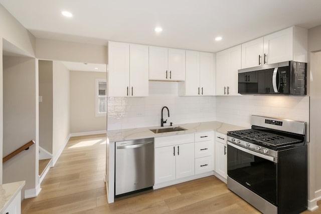 kitchen with light wood finished floors, light stone countertops, stainless steel appliances, white cabinetry, and a sink