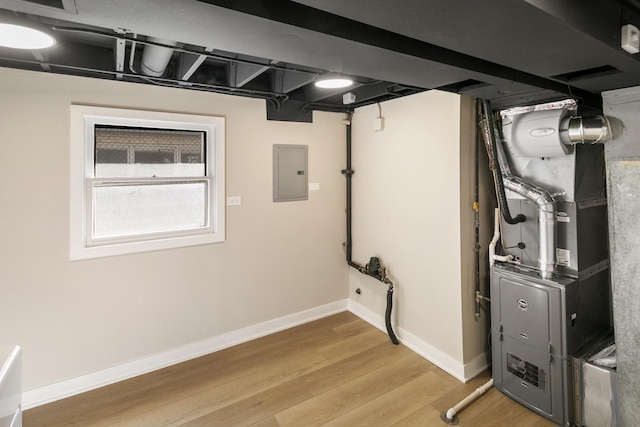 basement featuring light wood-type flooring, heating unit, electric panel, and baseboards