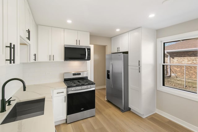 kitchen featuring white cabinets, light stone countertops, stainless steel appliances, and a sink