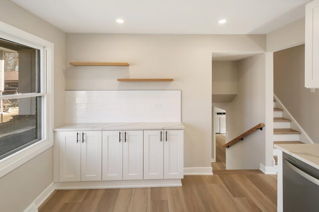 interior space featuring light stone counters, open shelves, stainless steel dishwasher, light wood-style floors, and white cabinetry